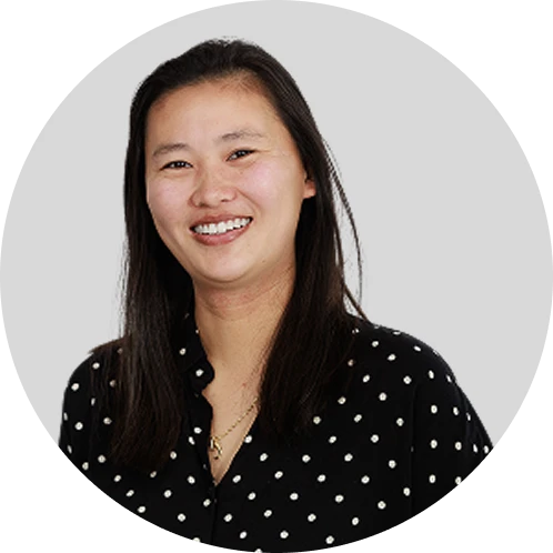 Kristina 1 - Lynk Diagnostics - Lynk Diagnostics Smiling woman with shoulder-length dark hair wearing a black polka-dot blouse, posed against a light gray circular background.